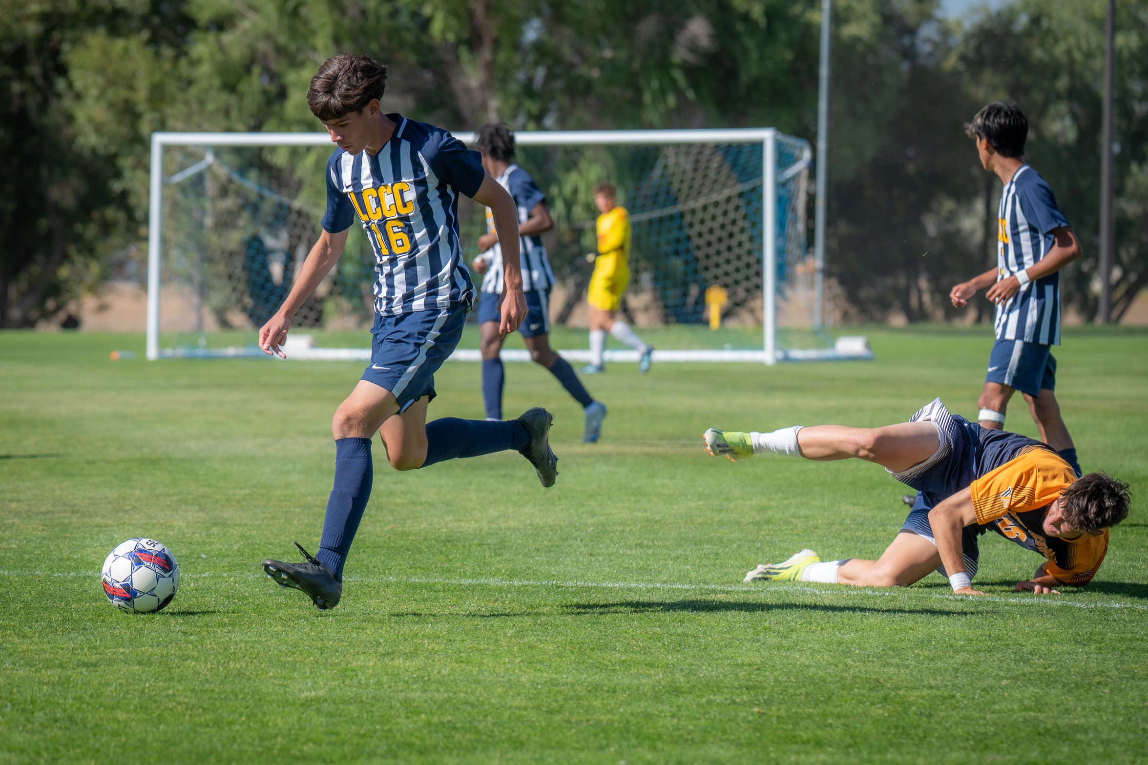 LCCC Player Dribbles past opponent who has fallen on the pitch. 